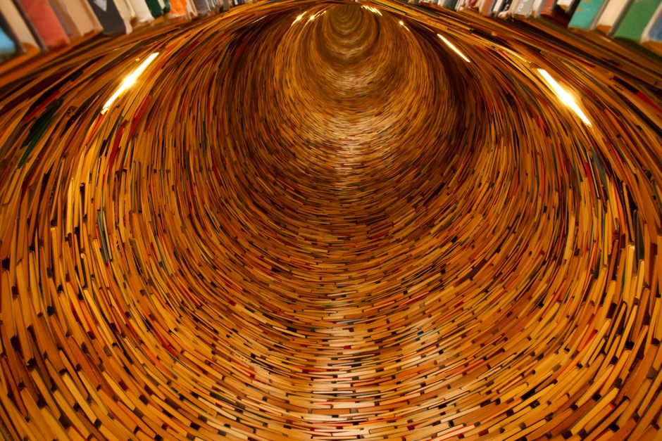 A mesmerizing tunnel of books creating an endless spiral effect in a library setting.