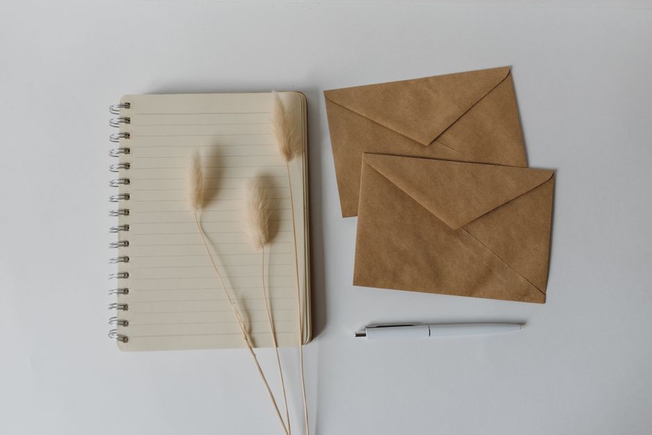 Flat lay image featuring a notebook, brown envelopes, and a pen on a white background. Perfect for mockups.